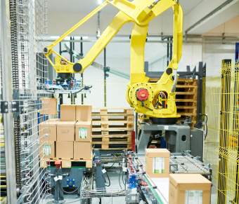 Large yellow robotic arm moving boxes from conveyor to pallet in warehouse