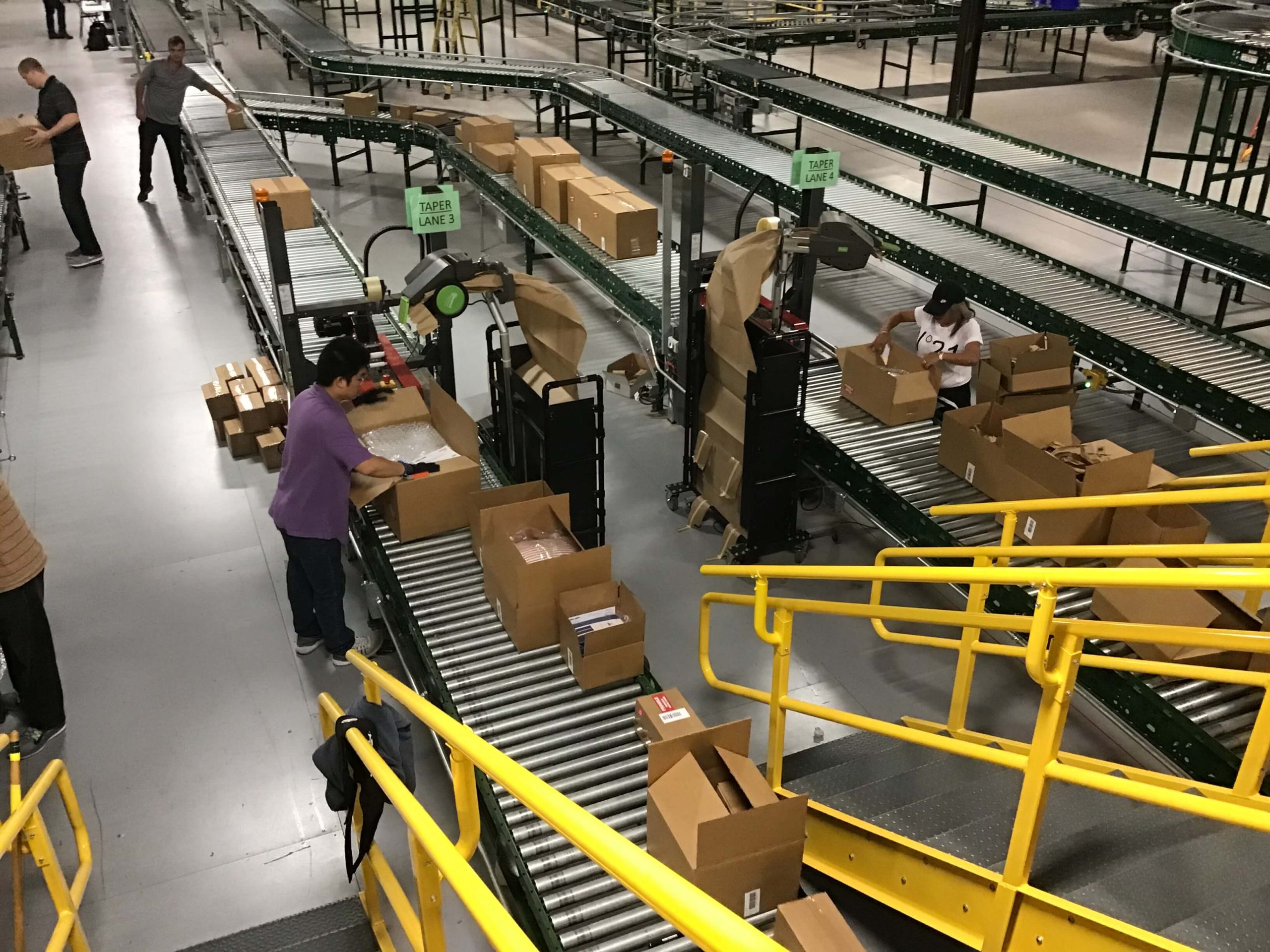 Workers filling cardboard boxes with paper on a conveyor line in warehouse