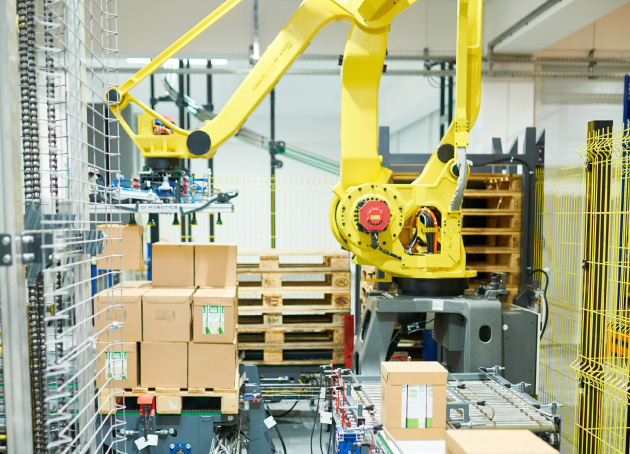 Large yellow robotic arm placing boxes from conveyor onto pallet
