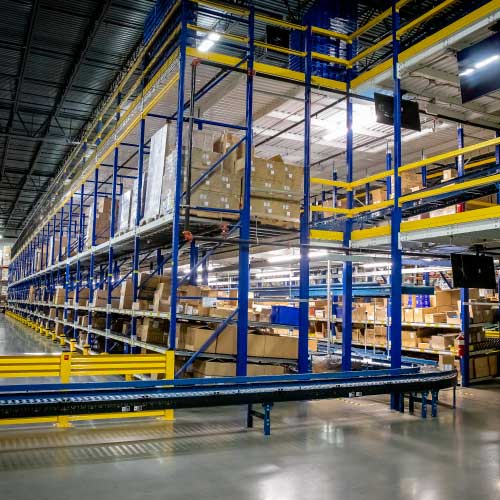 Three levels of blue storage racking and conveyor running beween aisles