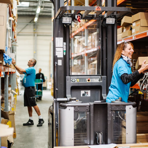 Woman and man in blue shirts in warehouse picking boxes from shelf