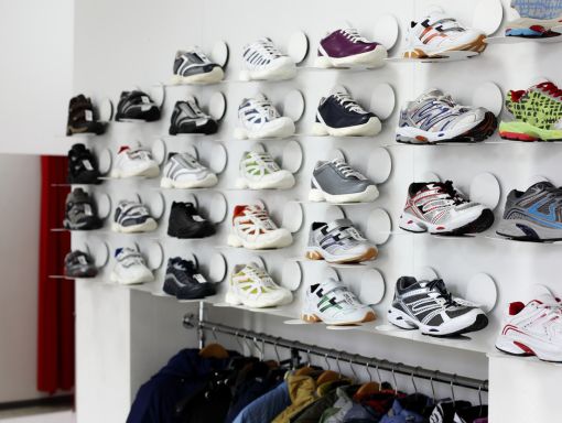 Gym shoe display on white wall above rack of clothing items