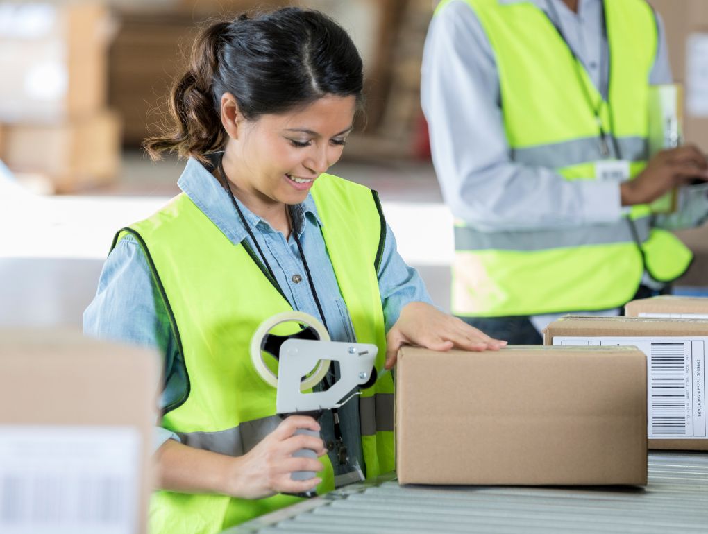 Woman in yellow safety vest using tape to seal package